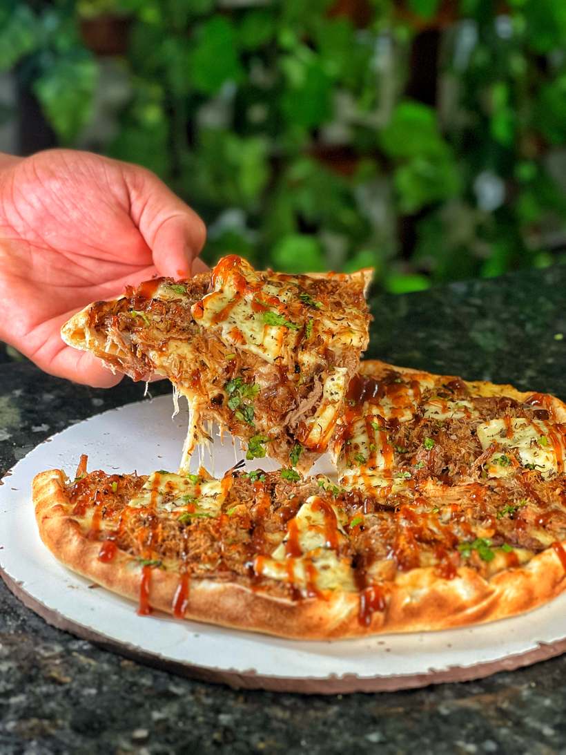 Fatia de pizza com carne desfiada e molho barbecue sendo puxada