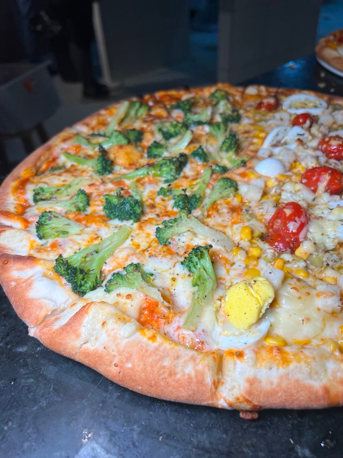 Pizza com brócolis de um lado e ovo de codorna, milho e tomate do outro